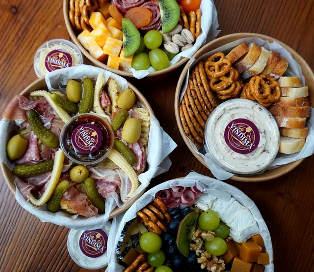Cuatro cajas para llevar con charcutería, quesos, encurtidos y fruta.