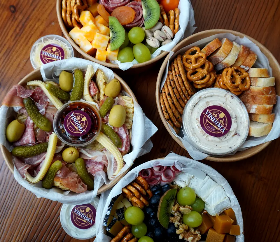 Cuatro cajas para llevar con charcutería, quesos, encurtidos y fruta.