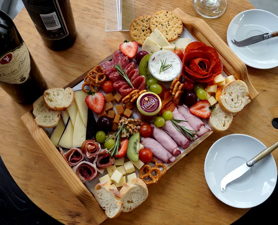 Tabla en bandeja de madera, servida para dos, con vino y platos puestos.